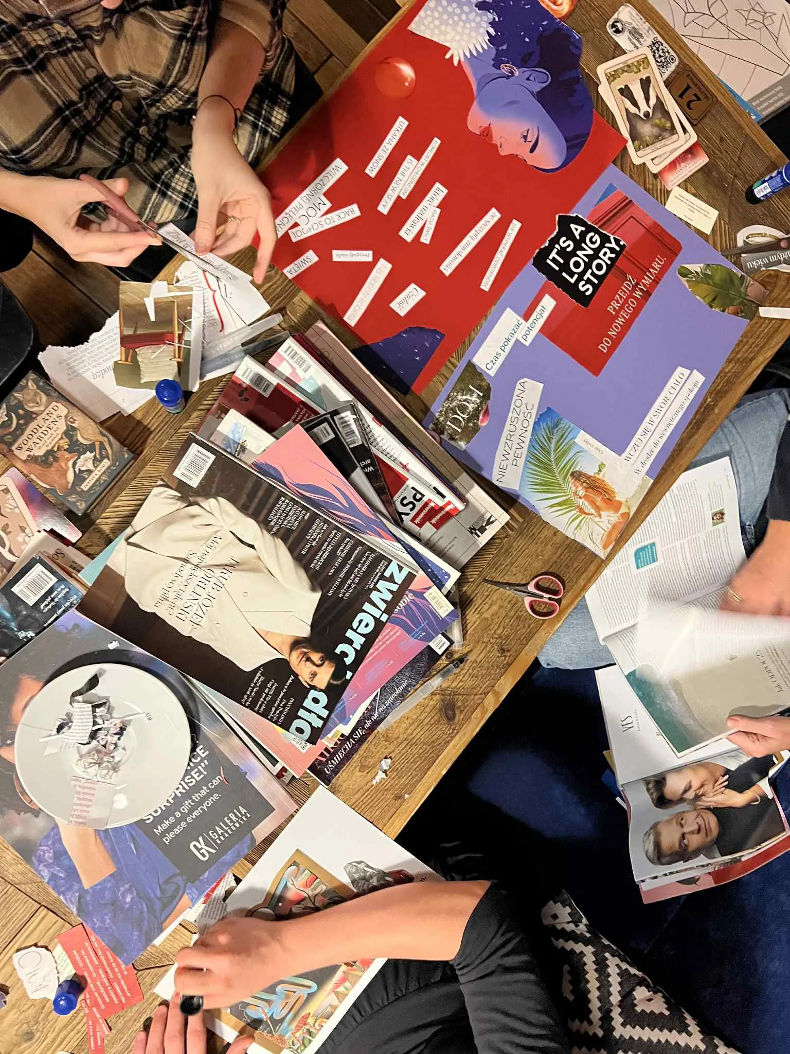 Osoby układają wycinki z magazynów na dużym, kolorowym kolażu.